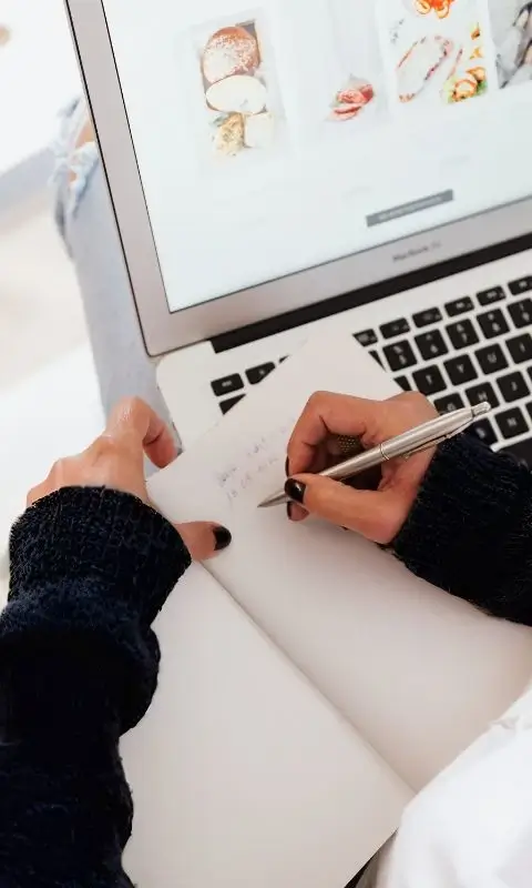 Kobieta notująca coś w notesie przy laptopie